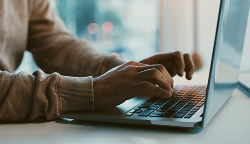 Lady looking at phone and transferring data into laptop, coffee cup on her desk