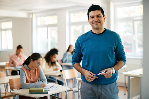 Teacher looking at camera holding a pen whilst students head down and working